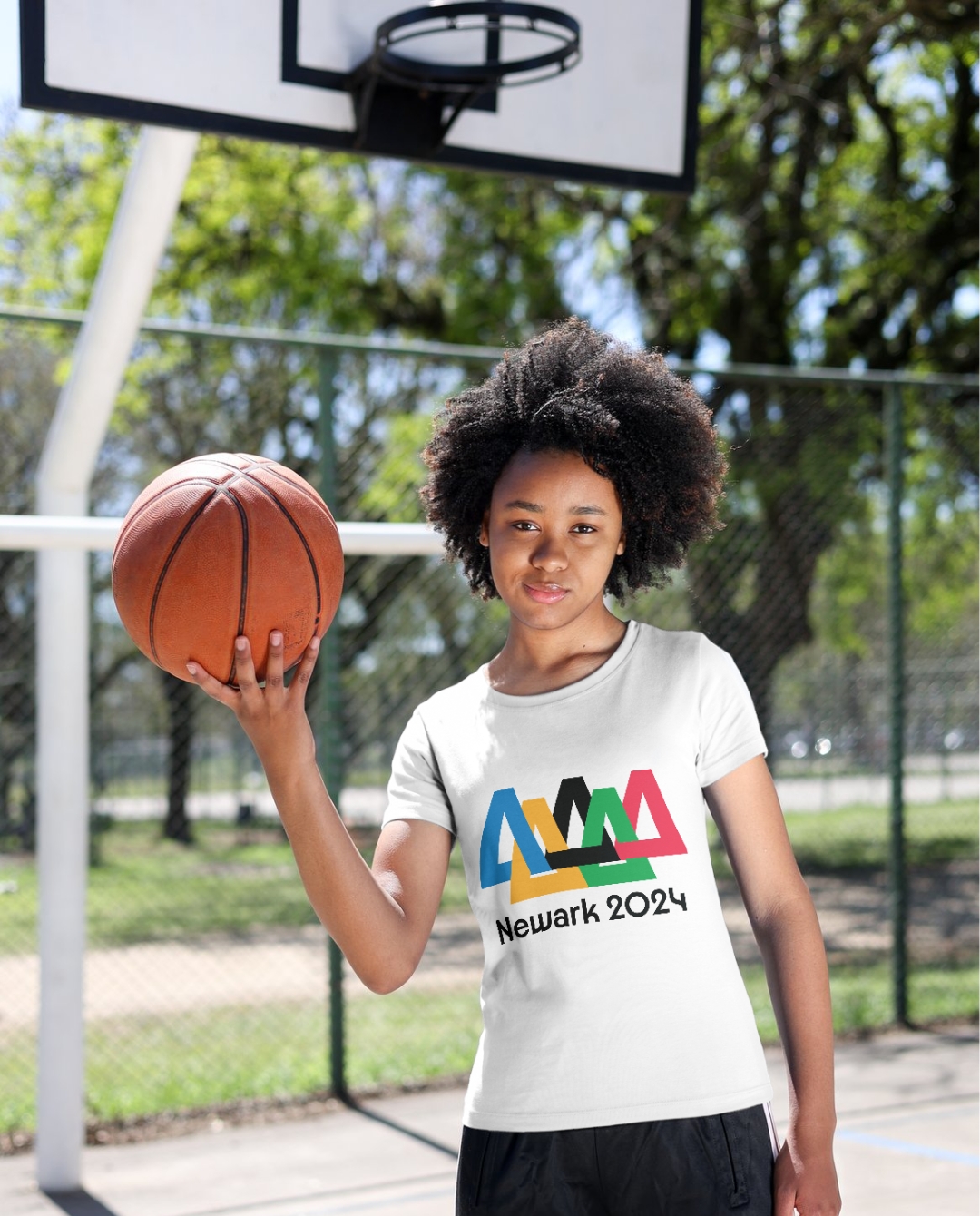 girl holding a basket ball in her right hand in a basketball court wearing the Newark 2024 capsule collection tshirt